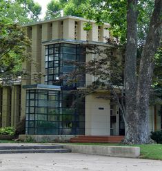 a large building sitting next to a tree on top of a cement block sidewalk with steps leading up to it