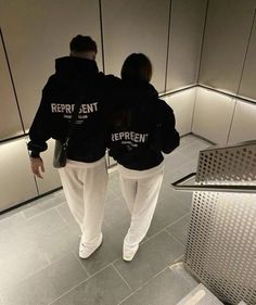 two people in black sweatshirts walking down an escalator with their backs to the camera