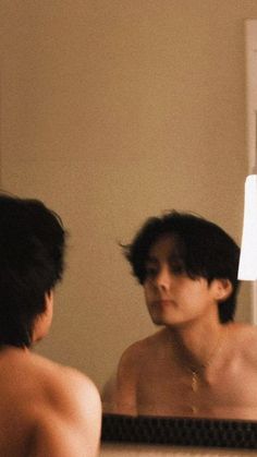 a shirtless man looking at himself in the mirror