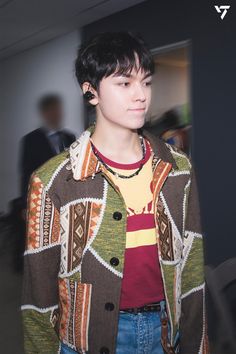 a young man with black hair wearing a multicolored jacket