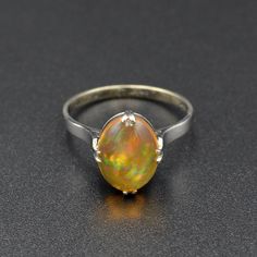 "A rainbow is swimming in this gorgeous antique opal ring! A beautifully proportioned opal cabochon is centered with cardinal prongs (north, south, west and east) in an 18k white gold setting. The opal features a transparent orange body, typical of Mexican jelly opals, with a \"contra luz\" color flash seen when the gem interacts with light. The color play is astounding, with every color of the rainbow ignited within the body of the opal, having painterly brush-stroke like patterns. This ring hails from the 1920s and has been tenderly well-cared for in its lifetime. It is in wonderful condition and ready for a new owner. This ring could be a perfect alternative engagement ring, gift for someone with an October birthstone or simply a present for an antique jewelry lover.   Opal is a fascina Oval Cabochon Opal Ring With Polished Finish, Fine Jewelry Oval Cabochon Opal Ring, Oval Cabochon Opal Ring Fine Jewelry, Oval Cabochon Opal Ring In Fine Jewelry, Cabochon Yellow Gold Opal Ring Collectible, Yellow Gold Cabochon Opal Ring Collectible, Classic Ethiopian Opal Gemstone Rings, Yellow Gold Opal Cabochon Ring, Classic Opal Ring With Polished Oval Cabochon