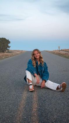 a woman sitting in the middle of an empty road