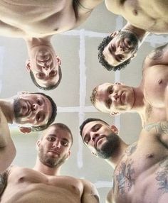 a group of men standing in a circle looking up at the camera with their shirts off