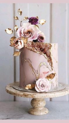 a pink cake with gold leaf and flowers on top is sitting on a small stand