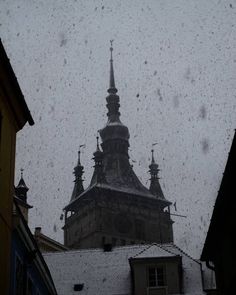 an old building with a steeple in the background and snow falling down on it