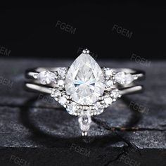 a white gold ring with a pear shaped diamond surrounded by smaller round brilliant cut diamonds