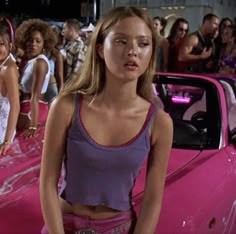 the girl next door is standing in front of her pink car and other girls are looking on