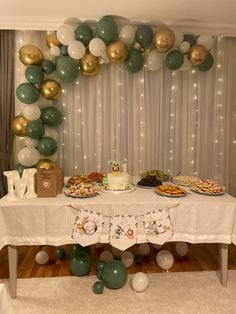 a table that has some food on it and balloons hanging from the wall behind it