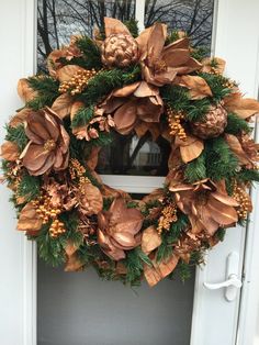 a wreath is hanging on the front door with pine cones and evergreens around it