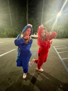 two girls dressed in costumes standing in a parking lot at night with their hands up