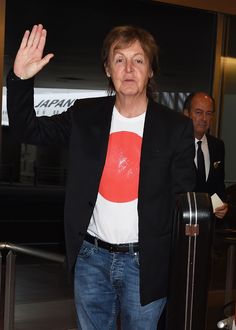 an older woman is waving and holding her hand up in the air as she stands next to luggage