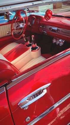 the interior of an old red car with chrome trim and steering wheel hubs is shown