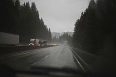 two trucks driving down the road on a rainy day with trees in the back ground