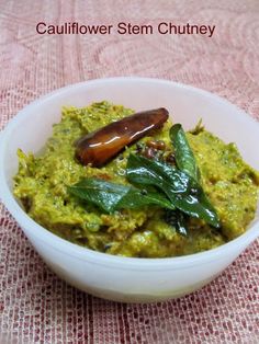 a white bowl filled with green food on top of a pink table cloth next to a wooden spoon