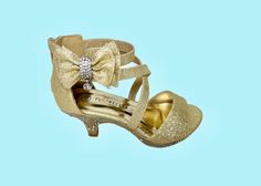 Beautiful strappy crisscross kids high heel shoes with an ankle strap and zipper in the back. The state of the art gold fabric has glitter like sparkle. Lots of rhinestones on the outside edge and heel of the shoe platform. Beautiful double bow with rhinestones and a pendant adds even more glamour. Adjustable ankle strap has elastic strain relief for added comfort. The 1.5″ tapered heels are perfect for little girls. All man made material. Available in toddler and childrens sizes. Gold High Heel Sandals For Holiday, Gold Low Heel Holiday Heels, Gold Glitter Closed Toe Sandals, Gold Holiday Heels With Low Heel, Gold Glitter Heels With Round Toe, Gold Sandals With Glitter Accents For Formal Occasion, Gold Glitter High Heel Sandals, Gold High Heel Sandals With Glitter Accents, Girls High Heel Shoes