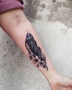 a black and white feather tattoo on the left inner arm with daisies around it