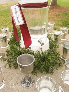 an assortment of silver dishes and cups on a table with a red ribbon around it