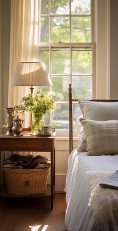 a bed sitting under a window next to a table with a lamp on top of it