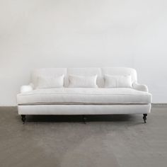 a white couch sitting on top of a cement floor next to a wall with three pillows