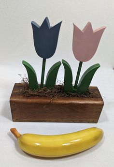 a banana and some paper flowers in a wooden box with grass on the ground next to it