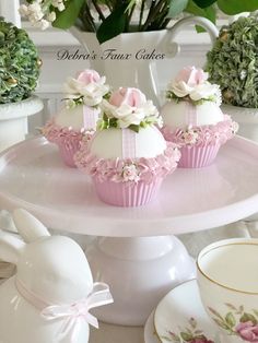 three pink cupcakes on a cake stand with flowers in the background and greenery