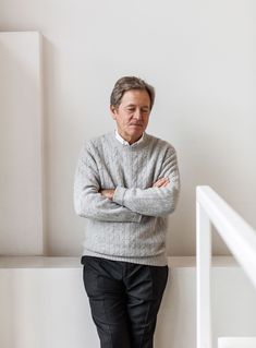 an older man standing in front of a white wall with his arms crossed and looking at the camera