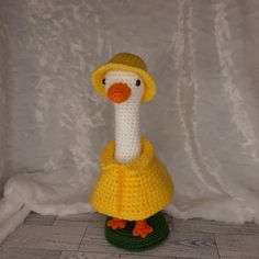 a crocheted stuffed bird wearing a yellow dress and hat on top of a green base