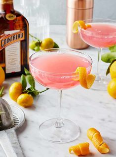 two cocktail glasses filled with pink lemonade and garnished with orange peels