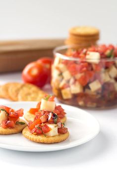 small appetizers with tomatoes, cheese and crackers on a white plate next to a glass jar