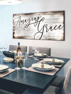 a dining room table with place settings and wine glasses on it, next to a large wooden sign that says amazing grace