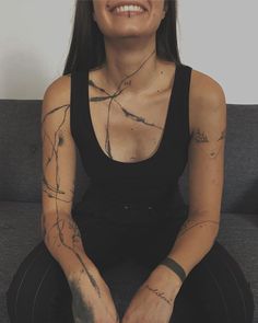 a woman sitting on top of a couch with tattoos on her chest and arms,