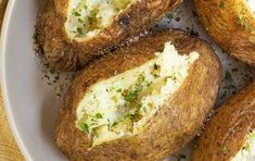 several baked potatoes with cheese and herbs in a bowl on a wooden table top, ready to be eaten