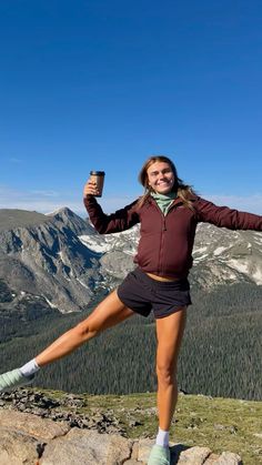 a woman posing on top of a mountain with her legs spread out and holding a cell phone