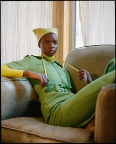 a woman sitting on top of a couch wearing green pants and a yellow head scarf