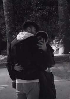 black and white photograph of two people hugging each other on the street with trees in the background