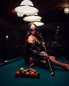 a beautiful woman sitting on top of a pool table in front of a light fixture