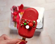 a person is holding a red popsicle decorated with christmas decorations and bows on it