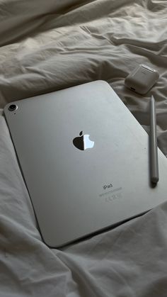 an apple laptop sitting on top of a bed next to a cell phone and pen