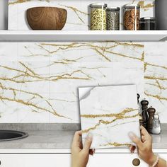 two hands holding papers in front of a white counter top with gold veining on it