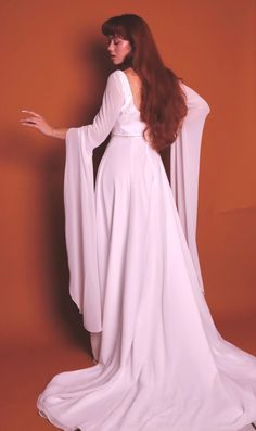 This is a stunning and rare 1960's fairytale renaissance vintage wedding dress - i have truly never seen one quite like this. it is a sleek white dress with two layers: a solid white underlay and a sheer white overlay. this zips closed in the back fitting the detailed beaded waist to your shape. the top of the dress is adorned with circle clusters of beads resembling a star or snowflake making this so lovely for a winter wedding. the true star is clearly the sleeves - they are long dramatic sheer draping sleeves that have very subtle flower clusters of sequins through out. this piece is in insane condition for age and does't show signs of wear. please note below for sizing and feel free to ask any questions you may have before purchasing.  brand bonny size 12 length front 60" length back 9 Elegant White Medieval Dress For Costume Party, Medieval White Dress For Costume Party, White Fitted Ethereal Dress, Medieval Style White Wedding Dress, Elegant White Medieval Wedding Dress, Medieval White Dress With Fitted Bodice, Vintage Floor-length Medieval Wedding Dress, White Long Sleeve Costume Gown, Elegant White Wedding Dress For Costume