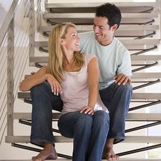 a man and woman sitting on the bottom of a stair case smiling at each other