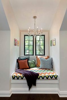 a window seat with pillows on it and a chandelier hanging from the ceiling