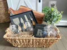 a basket with wine glasses and other items in it on the floor next to a potted plant