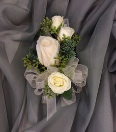 white roses and greenery are arranged on a gray fabric