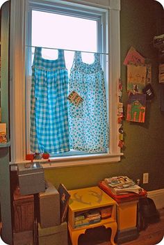 two children's dresses hanging on a window sill next to a toy table