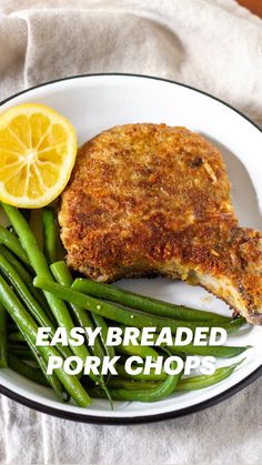 a white plate topped with meat and green beans next to a lemon wedge on top of a piece of bread