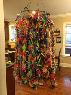 a room filled with lots of different colored paper cranes hanging from the ceiling over a hard wood floor