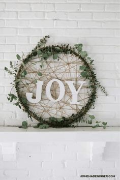 a wreath with the word joy is hanging on a white brick wall next to a sign that says joy