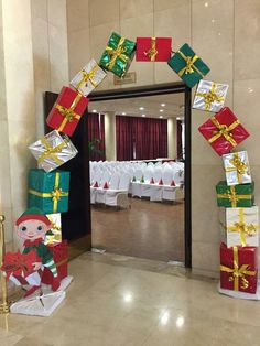 an arch made out of wrapped presents in a room with white tables and chairs set up for a christmas party