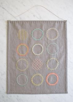 a gray wall hanging with different types of bracelets and rings on it's side